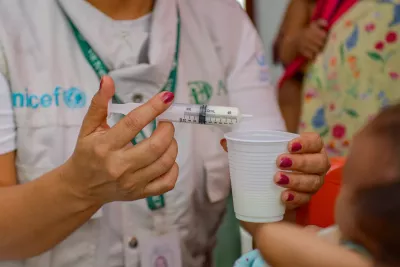 Mãos de uma mulher segurando uma seringa em uma mão e um copo de plástico na outra.